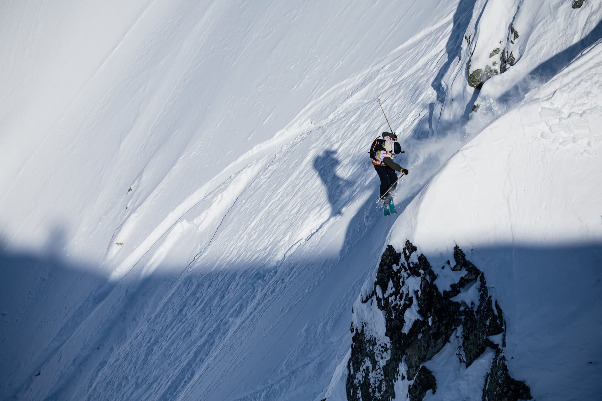 A skier on a steep sunlit face at the Georgia Pro, a shadow line cutting across the snow below